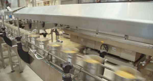 Cans moving in a food processing factory on a machine created by a food engineer